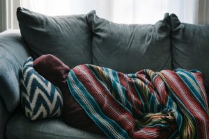 person wrapped in colorful blanket on gray couch